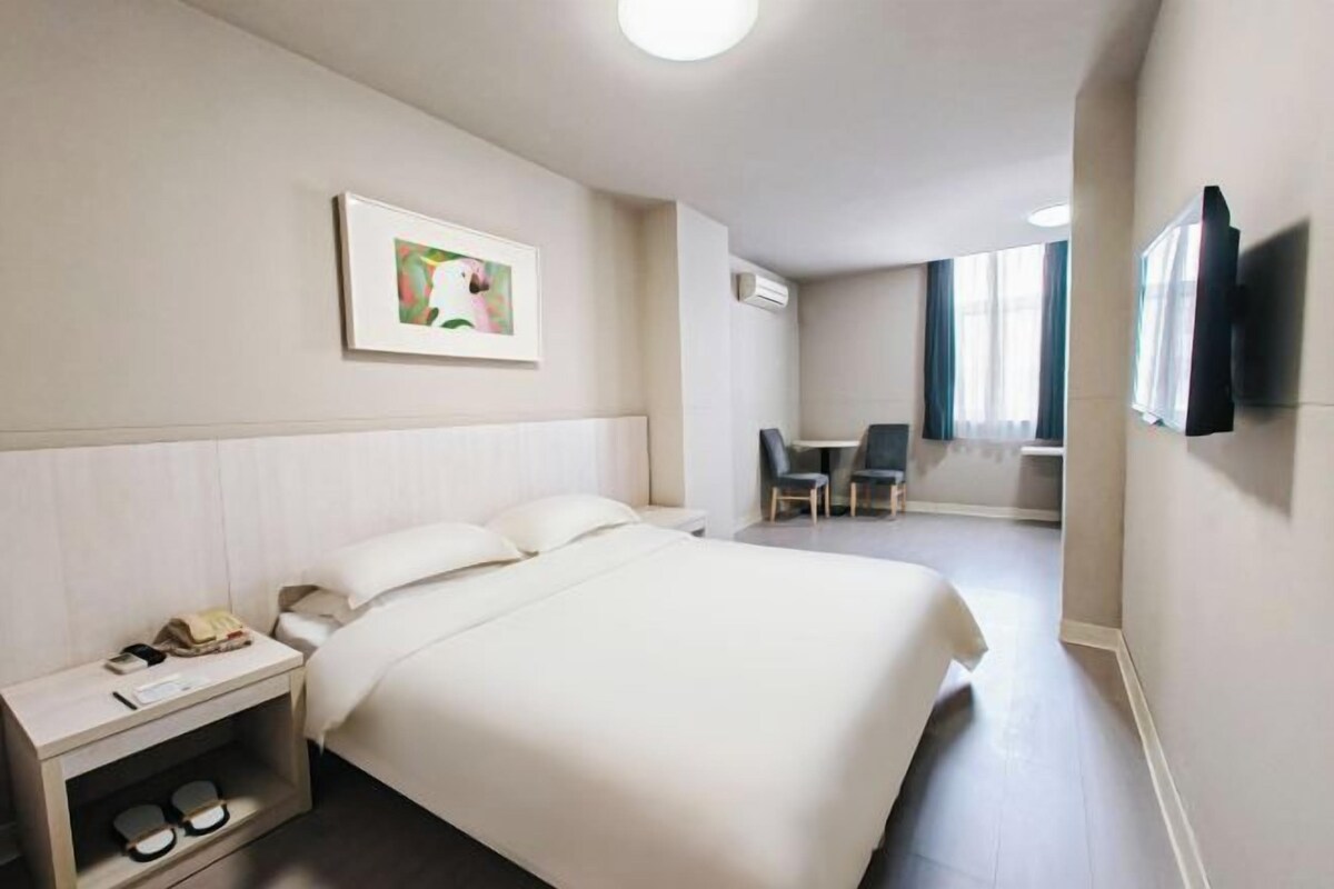 A hotel room with a bed, bedside table, chair, TV, and artwork on the wall.
