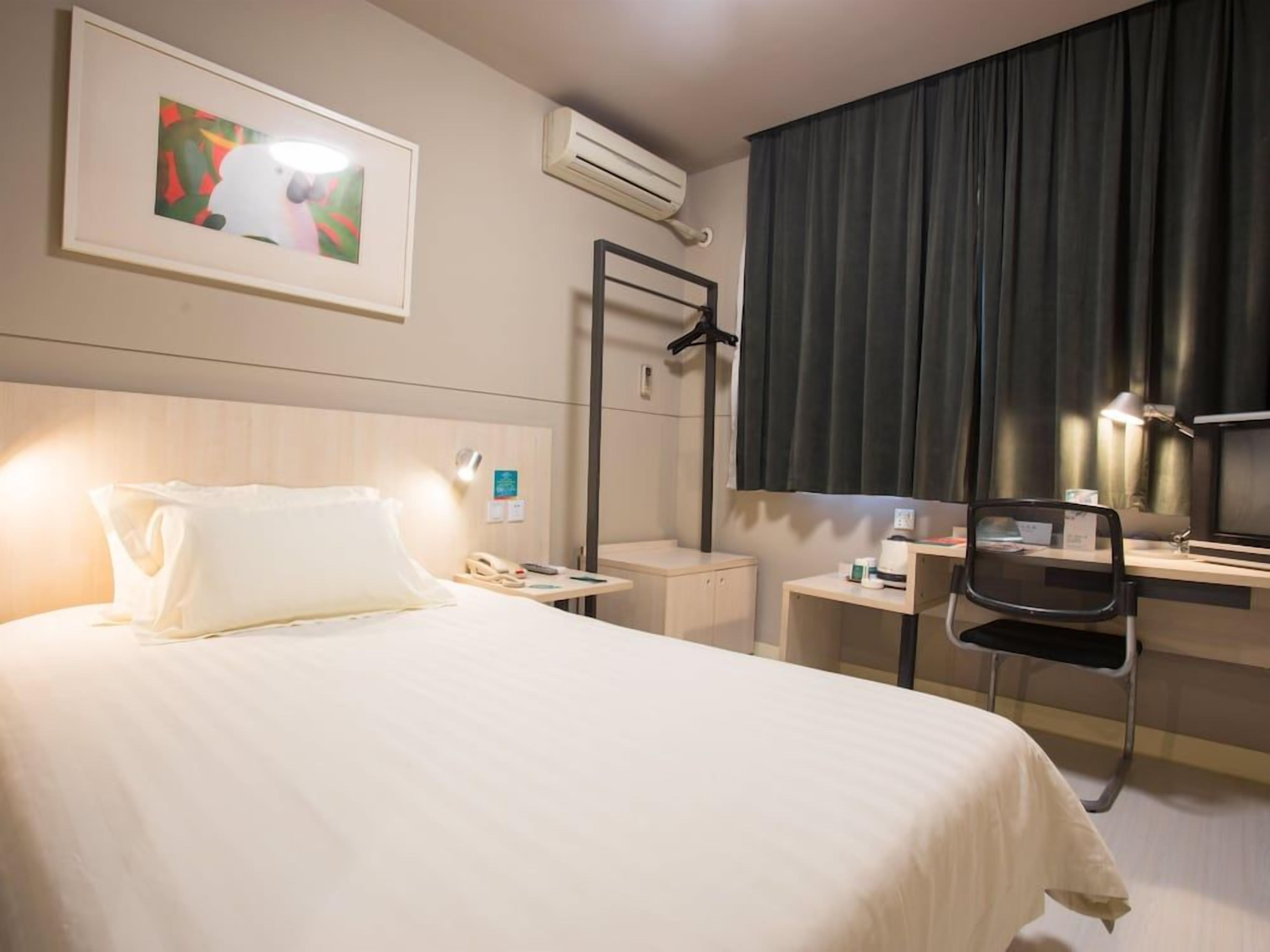 A hotel room with a bed, bedside table, chair, desk, and a painting on the wall.