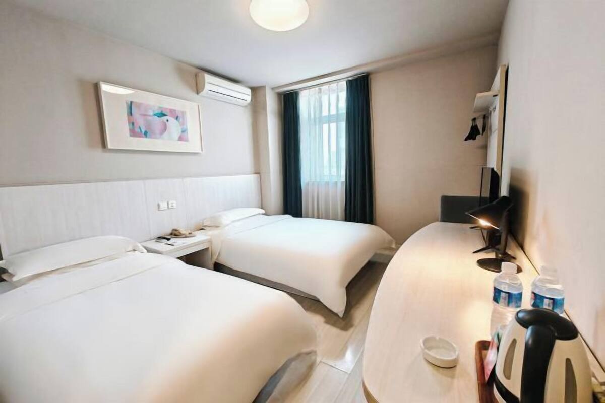 Habitación de hotel con dos camas, un escritorio con lámpara, un espejo y un cuadro en la pared.