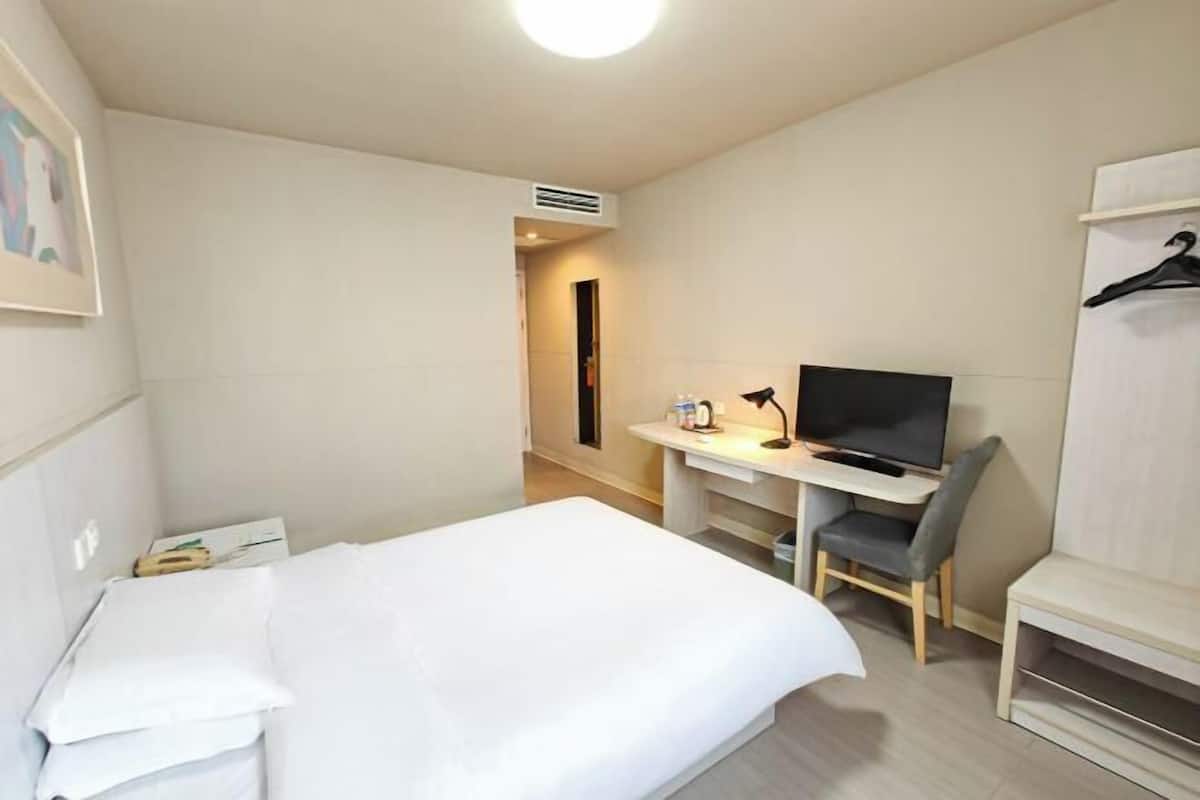 Una habitación de hotel con cama, escritorio con silla, televisión y armario.