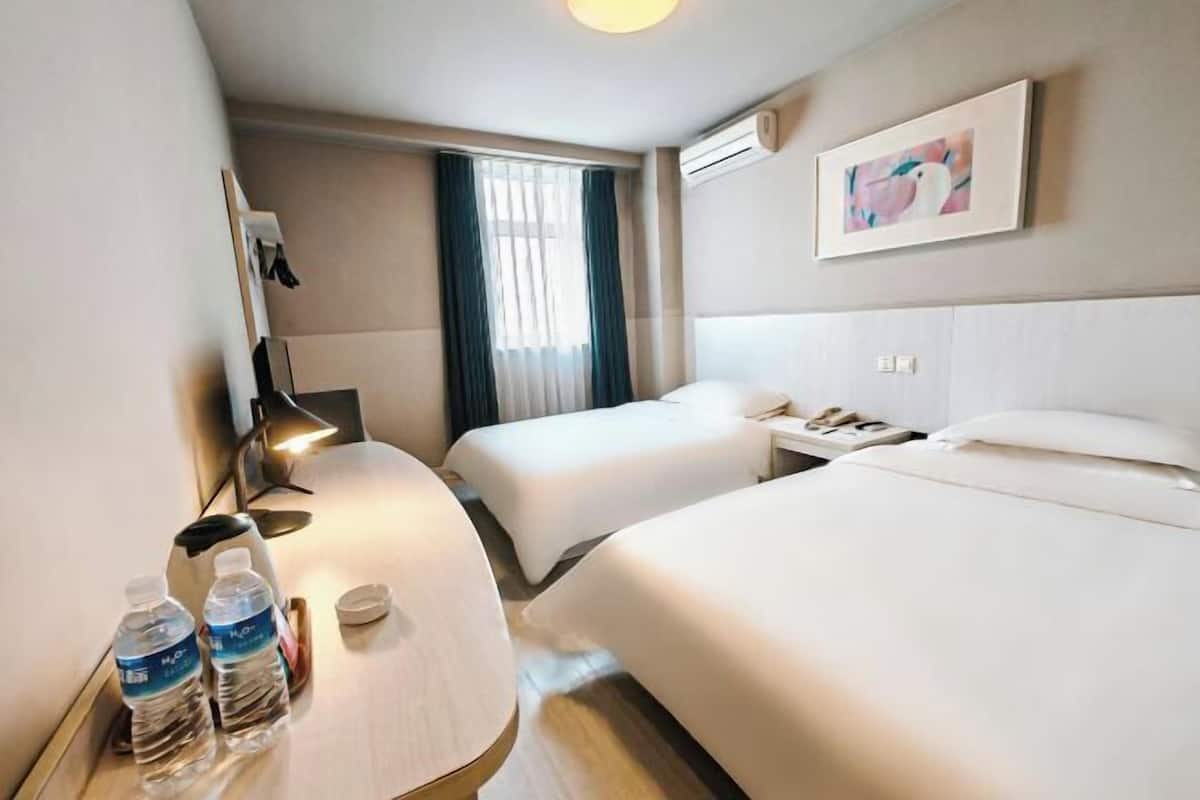 Una habitación de hotel con dos camas, un escritorio con lámpara, una botella de agua y un cuadro en la pared.