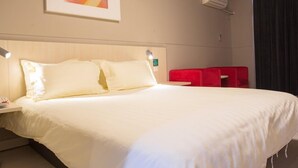 A hotel room with a large bed, a nightstand, a red chair, a wall-mounted air conditioner, and a framed picture above the bed. - Jinjiang Inn Shenyang North Station (Shenyang)