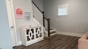 Un amplio salón con suelo de madera, una escalera y un ventanal pequeño.