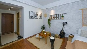 Een woonkamer met een witte bakstenen muur, een houten deur, een kleine tafel met een plant, een trommel en een gitaar.