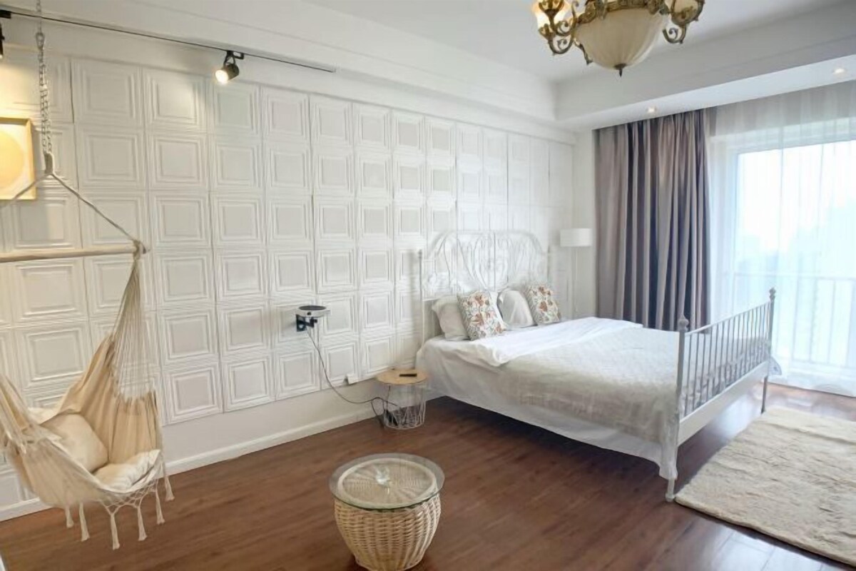 Un dormitorio con cama, una silla colgante, una mesita y una lámpara decorativa.
