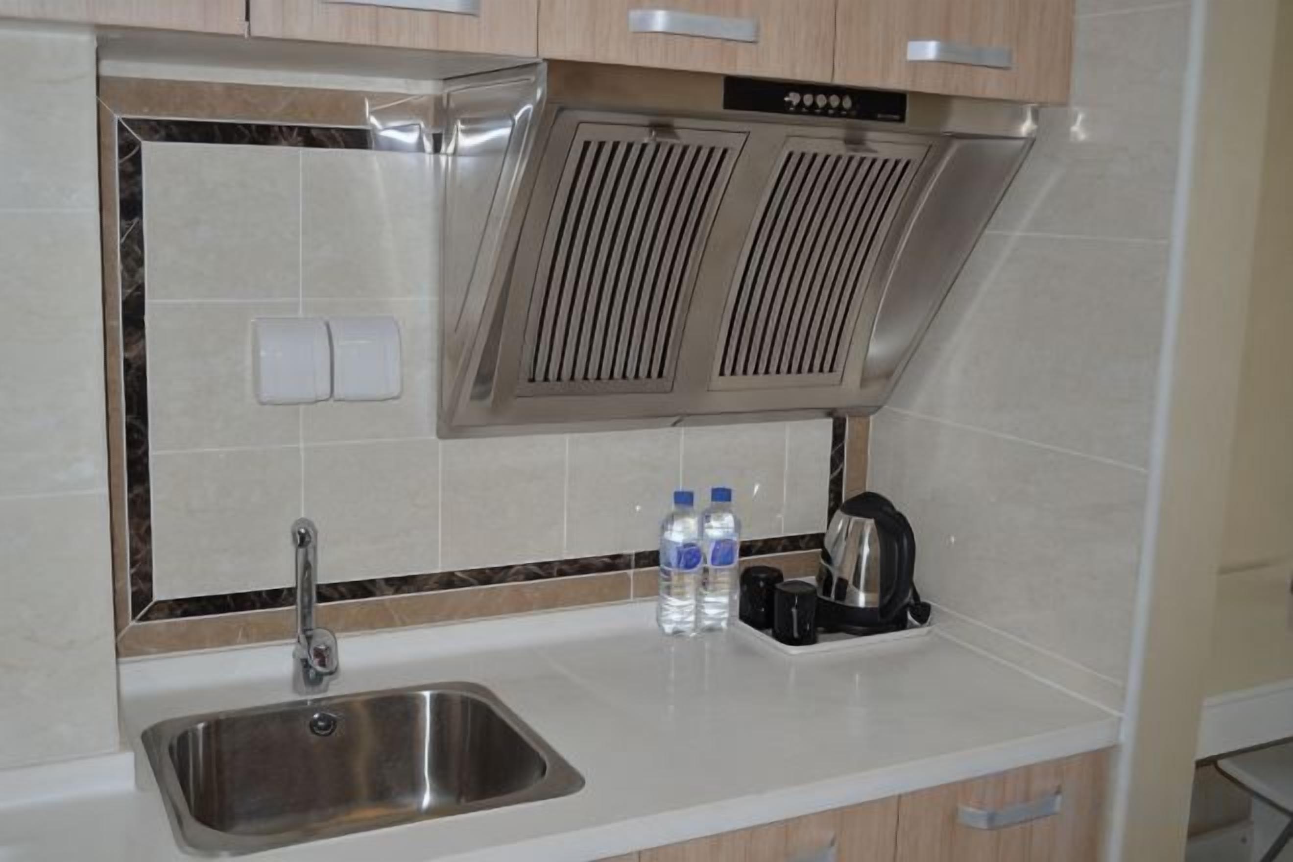 A kitchen with a stainless steel sink, two water bottles, a kettle, and a microwave.