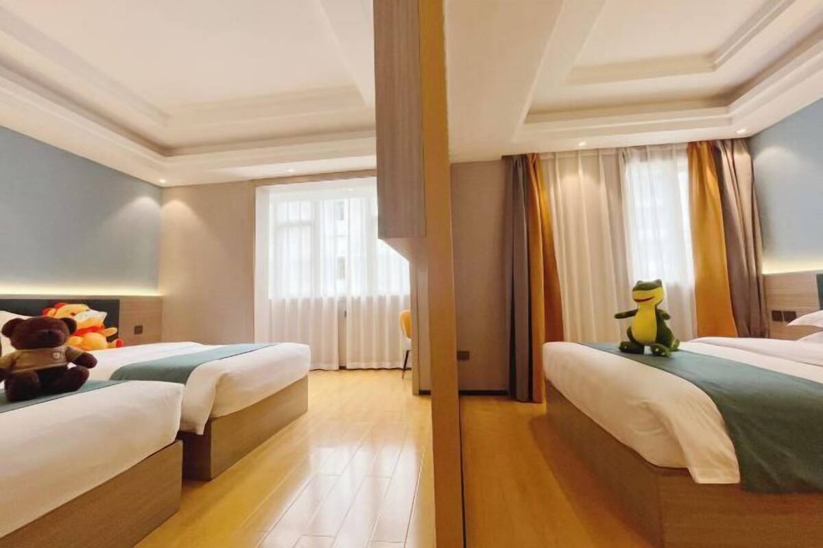 Een hotelkamer met twee bedden, een groot raam met gordijnen, en een zacht knuffelbeestje op een van de bedden.