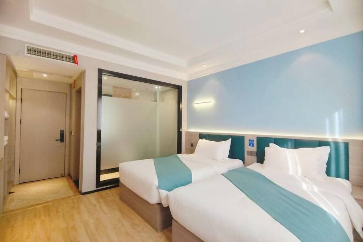 Hotelkamer met twee bedden, een schuifdeur, een grote spiegel en een blauwe accentmuur.