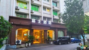 Entrada de hotel com fachada marrom, portas de vidro e plantas em vasos.