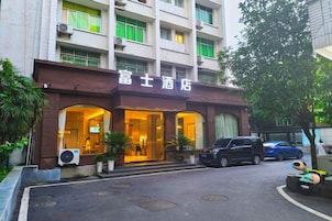 Fachada de hotel color café, con amplias ventanas y un estacionamiento frente a ella.