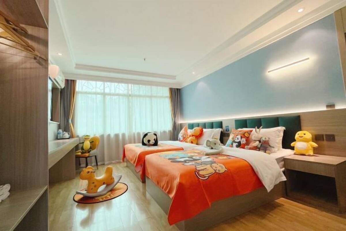 Een hotelkamer met twee bedden, een schommelpaard, een panda knuffel en een gele eend.
