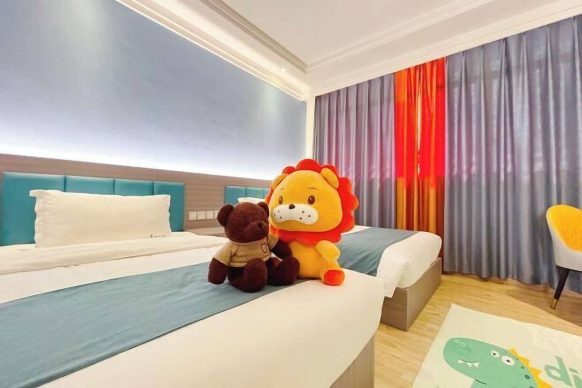 Een hotelkamer met een bed, een pluche leeuw, een pluizige beer en een kleurrijk vloerkleed.