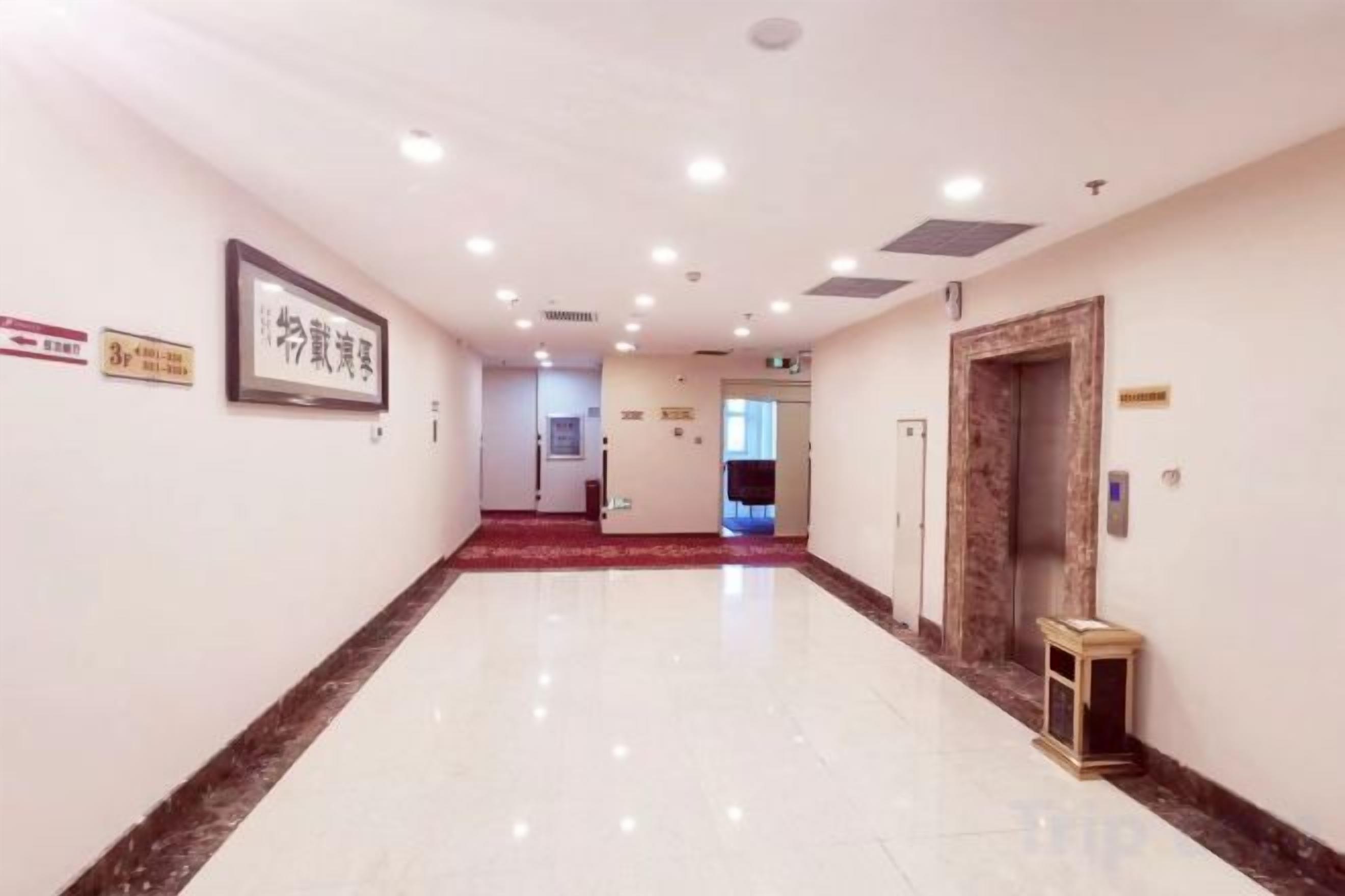 A hotel corridor with a polished floor, framed artwork, and a reception desk.