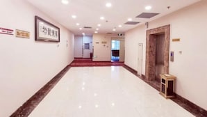 A hotel corridor with a polished floor, a framed sign on the wall, and a door with an elevator. - Jiangpan Business Hostel (Harbin)