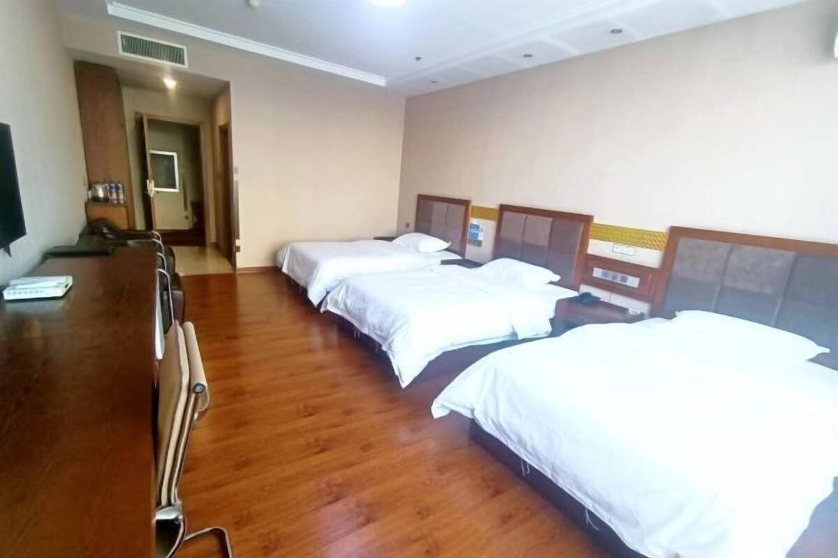 Une chambre d’hôtel avec trois lits simples, un bureau en bois et un téléviseur.