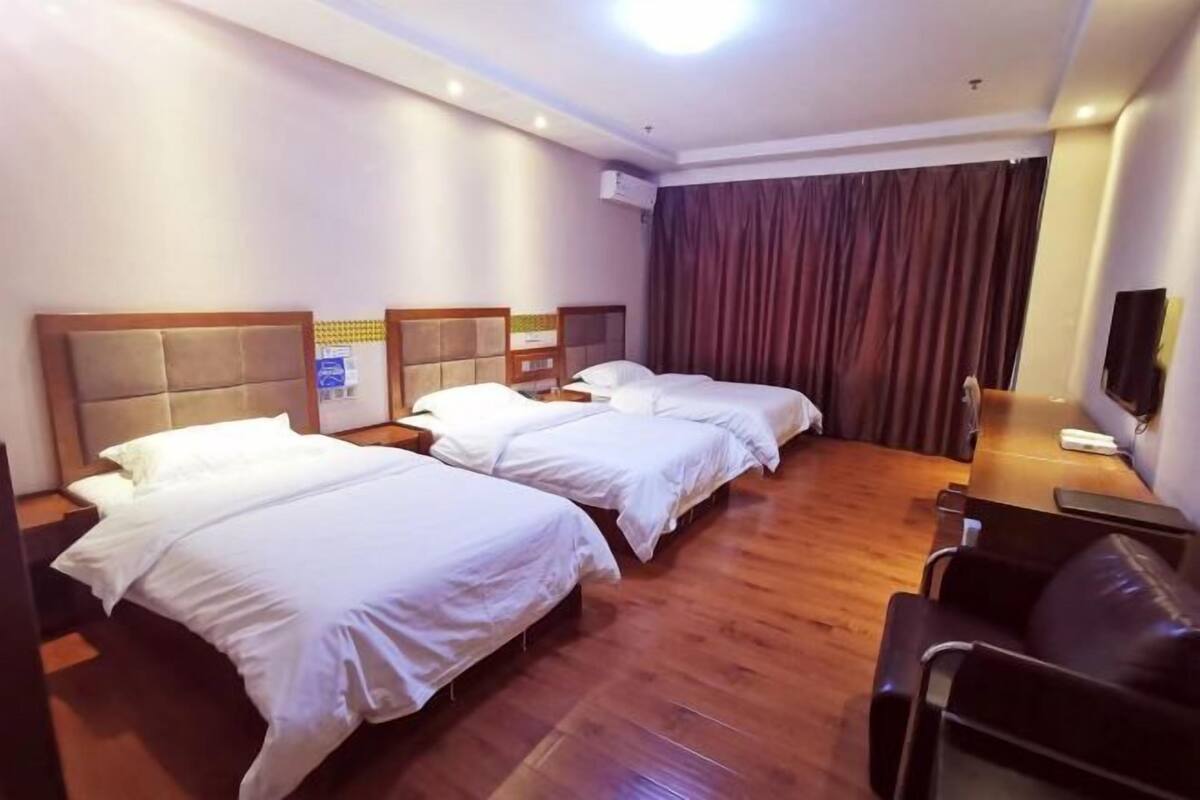 Une chambre d’hôtel avec trois lits, un plancher en bois, une télévision et un rideau.