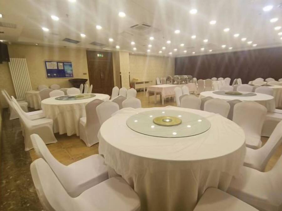 Un salón de banquetes con mesas redondas, sillas blancas y una zona escenario.