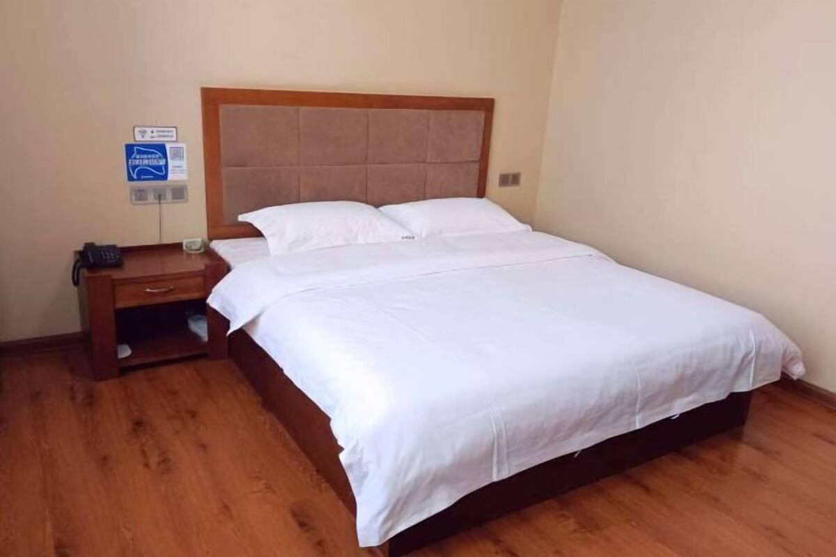 Un lit simple avec une tête de lit en bois, une table de chevet avec un téléphone et un panneau fixé au mur.