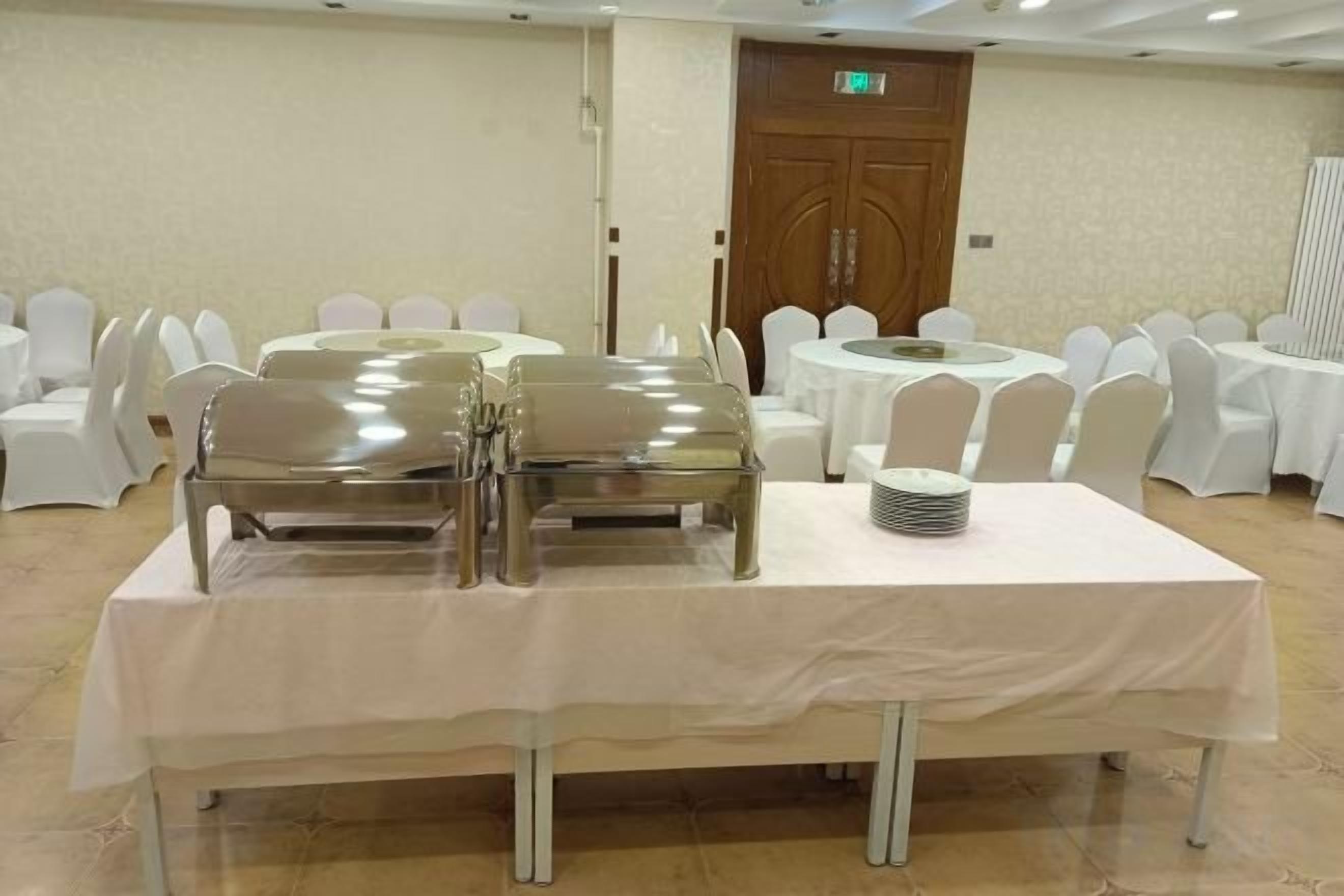 A banquet table with a white tablecloth, surrounded by white chairs, in a room with a wooden door and white walls.