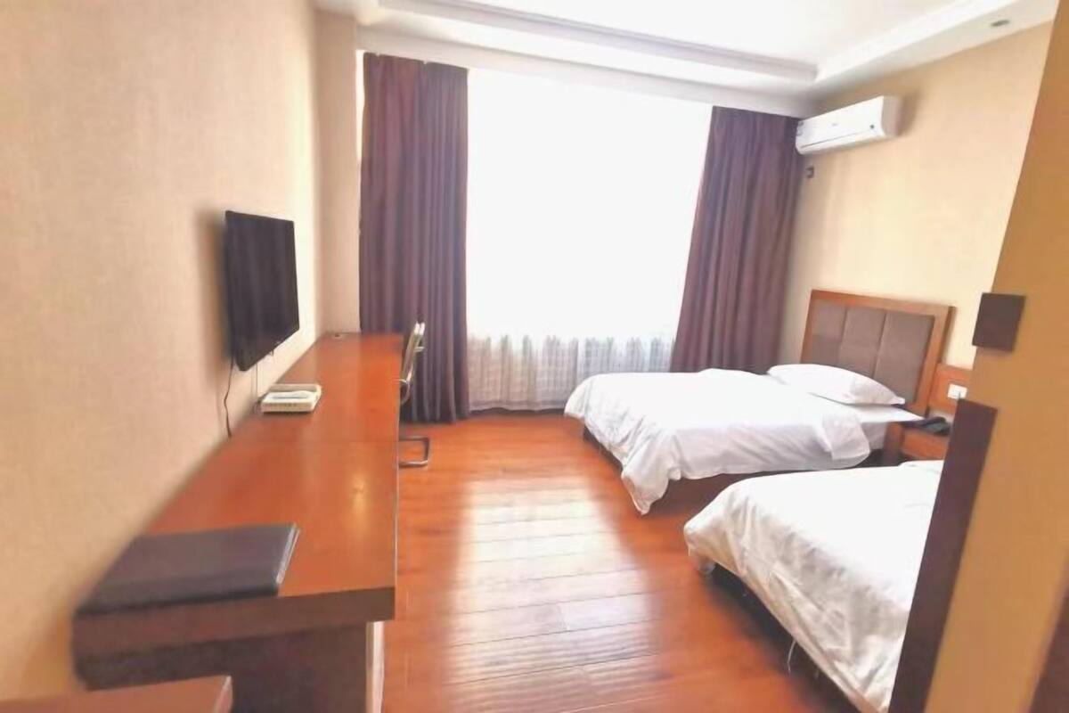 Une chambre d’hôtel avec un bureau en bois, deux lits, une télévision et un appareil de climatisation.