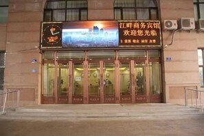 A hotel entrance with a large illuminated sign, glass doors, and a visible clock. - Jiangpan Business Hostel (Harbin)