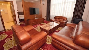 A hotel room with leather sofas, a wooden coffee table, a flat-screen TV, and a large window with curtains. - Jiangpan Business Hostel (Harbin)