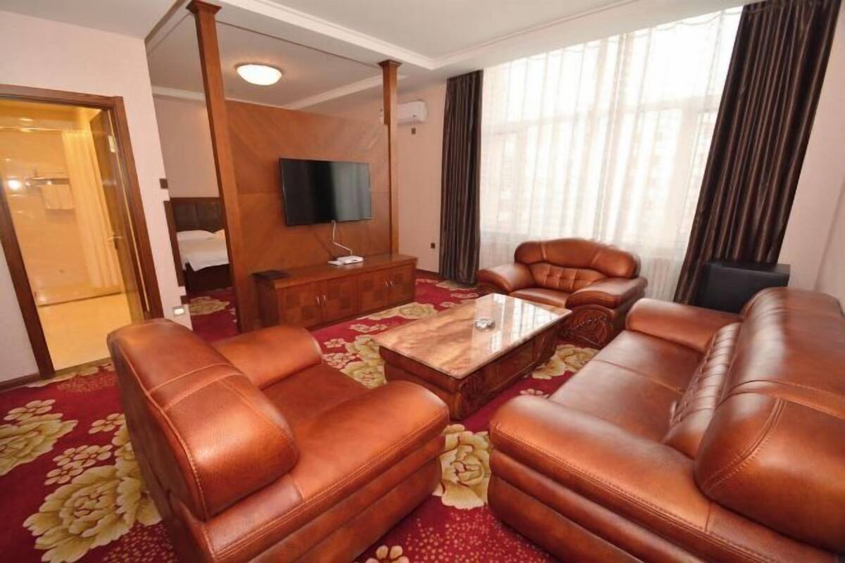 Une chambre d’hôtel avec des canapés en cuir, une table basse en bois, un t éléviseur à écran plat et une grande fenêtre avec des rideaux.
