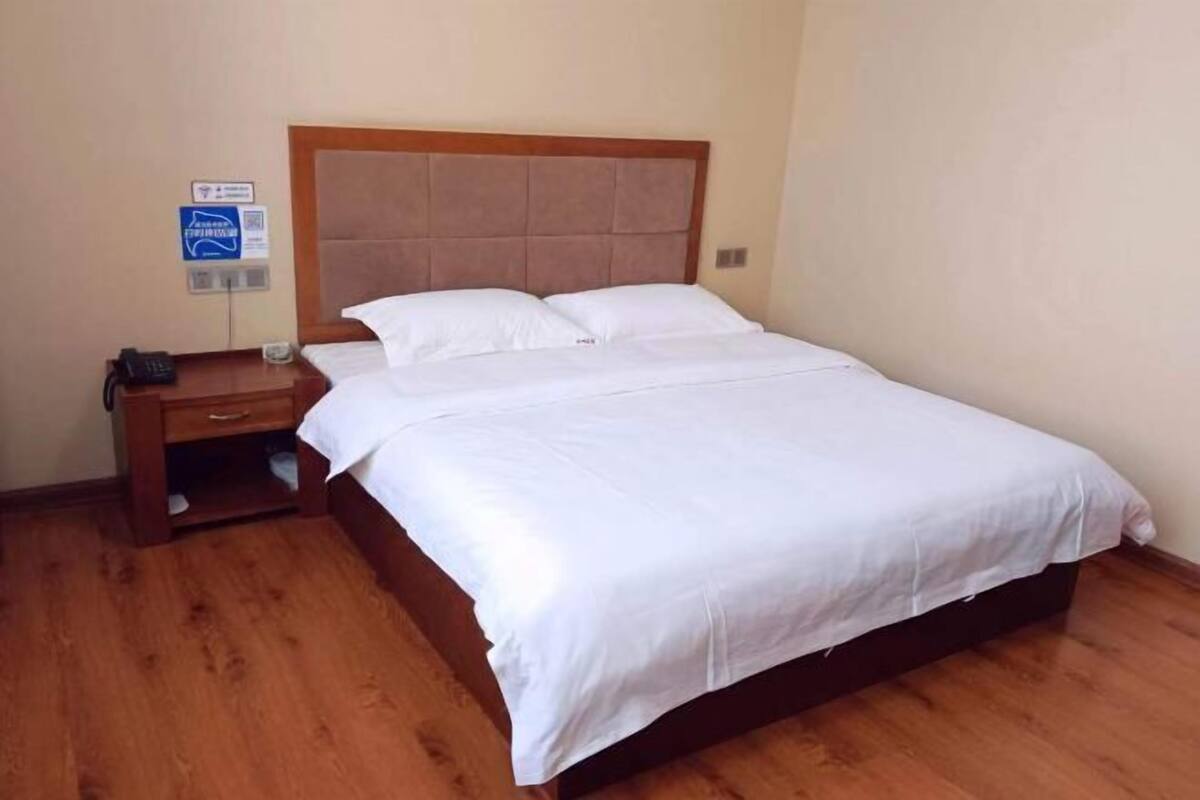 Un lit simple avec une tête de lit en bois, une table de chevet et une petite table de nuit avec un téléphone.