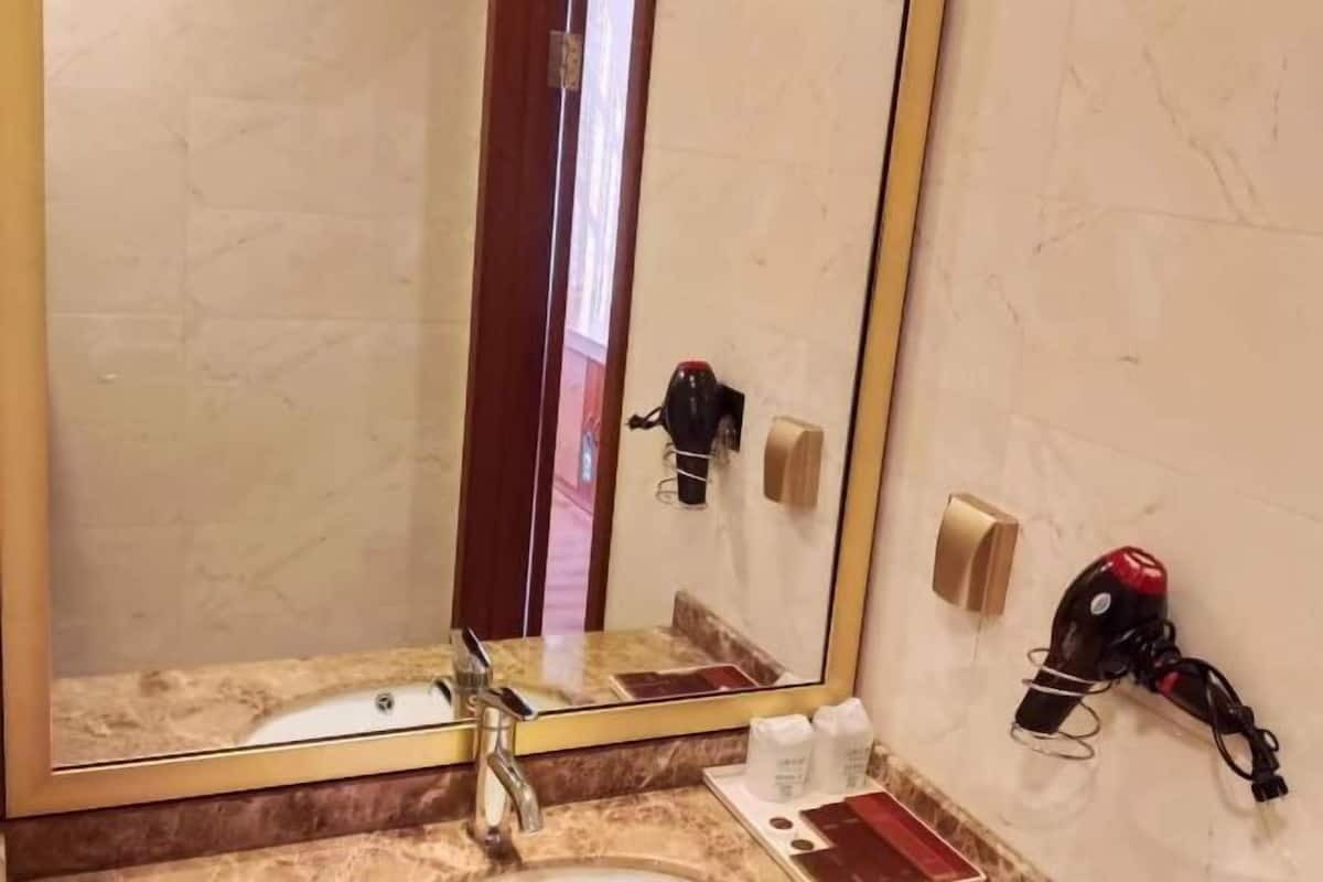 Une salle de bain avec un lavabo en marbre, un grand miroir et un sèche-cheveux fixé au mur.