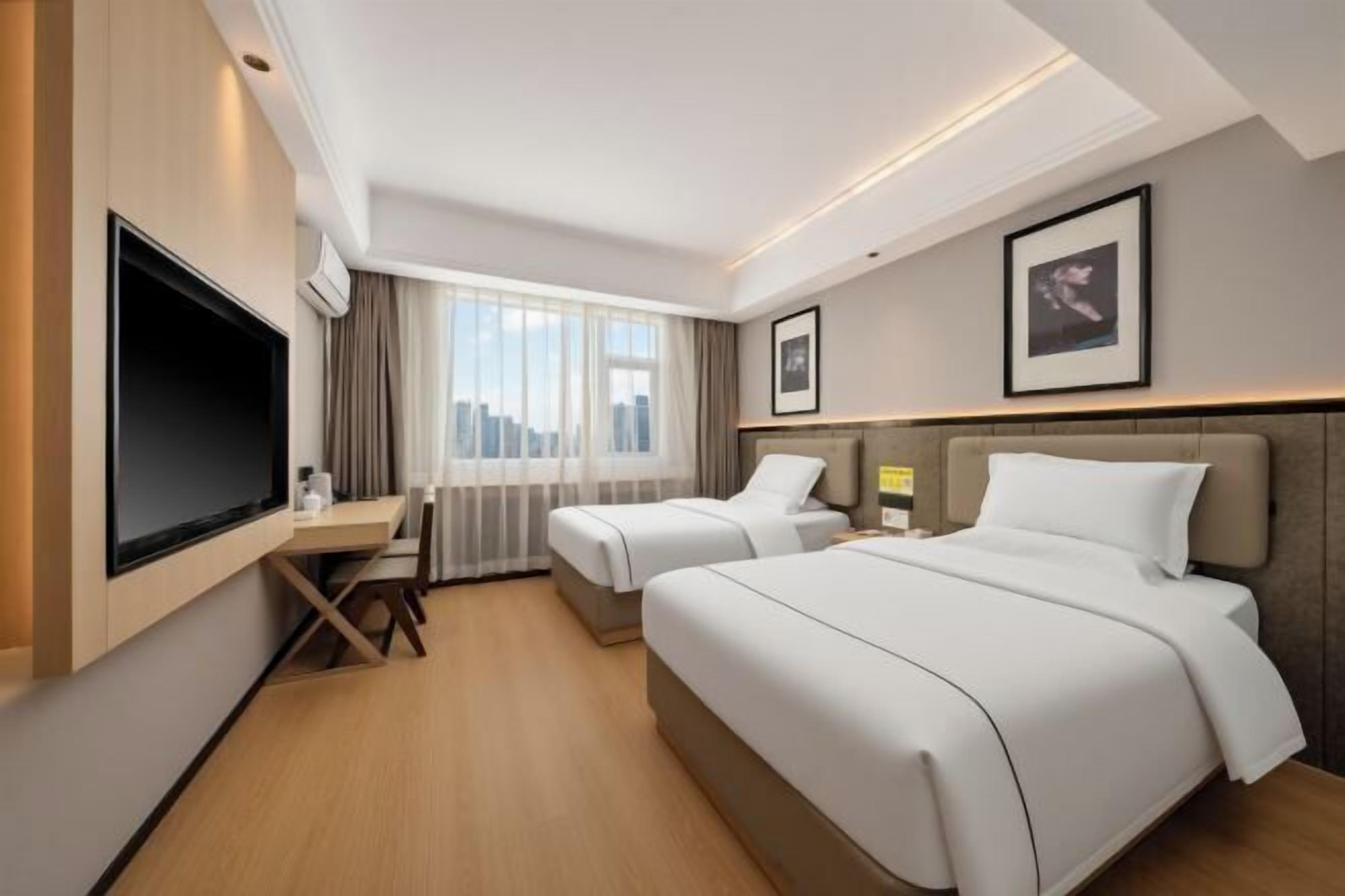 Ein Hotelzimmer mit zwei Betten, einem Schreibtisch, einem Flachbildfernseher und Blick auf die Stadt.