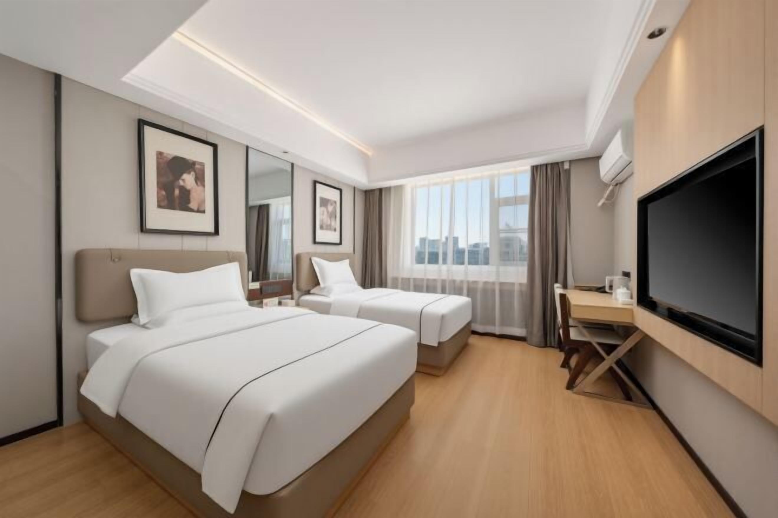 Ein Hotelzimmer mit zwei Betten, einem Schreibtisch, einem Flachbildfernseher und Blick auf die Stadt.