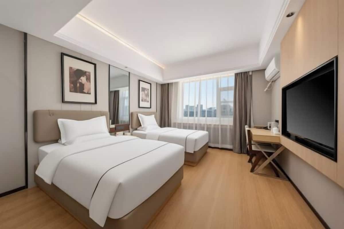 A hotel room with two beds, a desk, a flat-screen TV, and a city view.