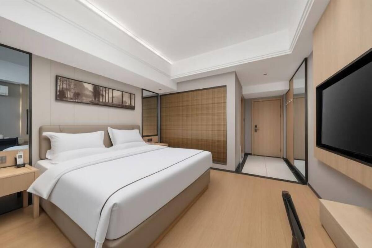 A modern hotel room with a large bed, bedside tables, a flat-screen TV, and a large mirror.