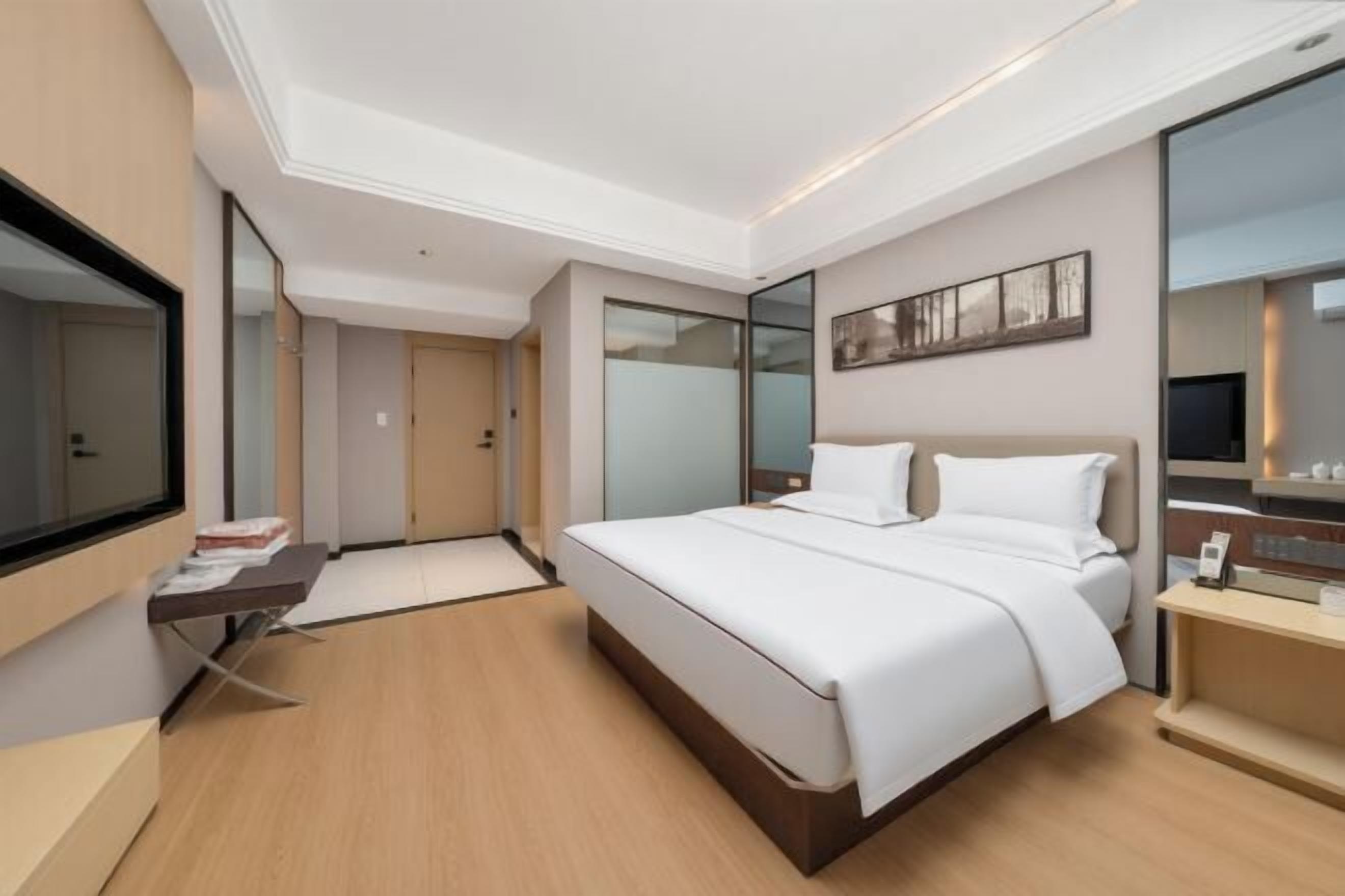 Ein modernes Hotelzimmer mit einem großen Bett, einem Schreibtisch, einem Flachbildfernseher und einem großen Fenster.