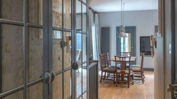 A modern interior with a wooden floor, a dining area with chairs and a table, and a large glass door with metal framing.