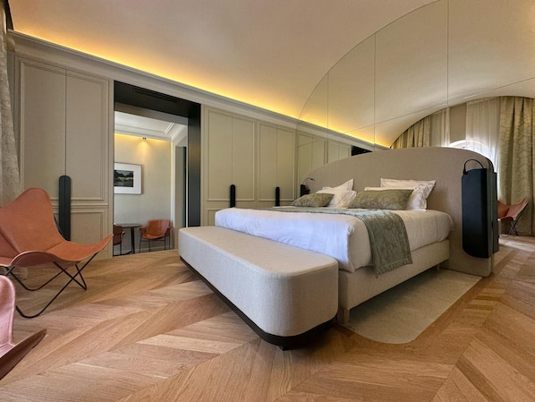 Ein modernes Hotelzimmer mit einem großen Bett, einer Sitzecke mit Stühlen und Blick auf die Stadt durch das Fenster.