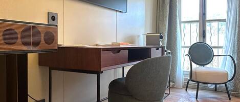 Una sala moderna con un televisor de pantalla plana montado en la pared, un escritorio de madera con una computadora, un sillón gris y una ventana con cortinas.