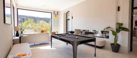 A modern room with a pool table, a comfortable seating area, and a large window offering a scenic view.