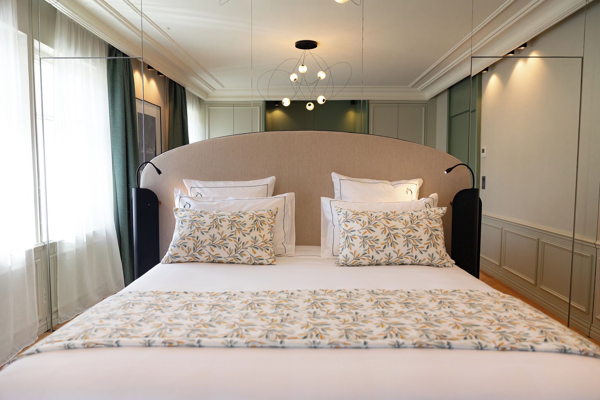 Quarto de hotel com uma cama grande, duas almofadas, mesa de cabeceira e um lustre moderno.