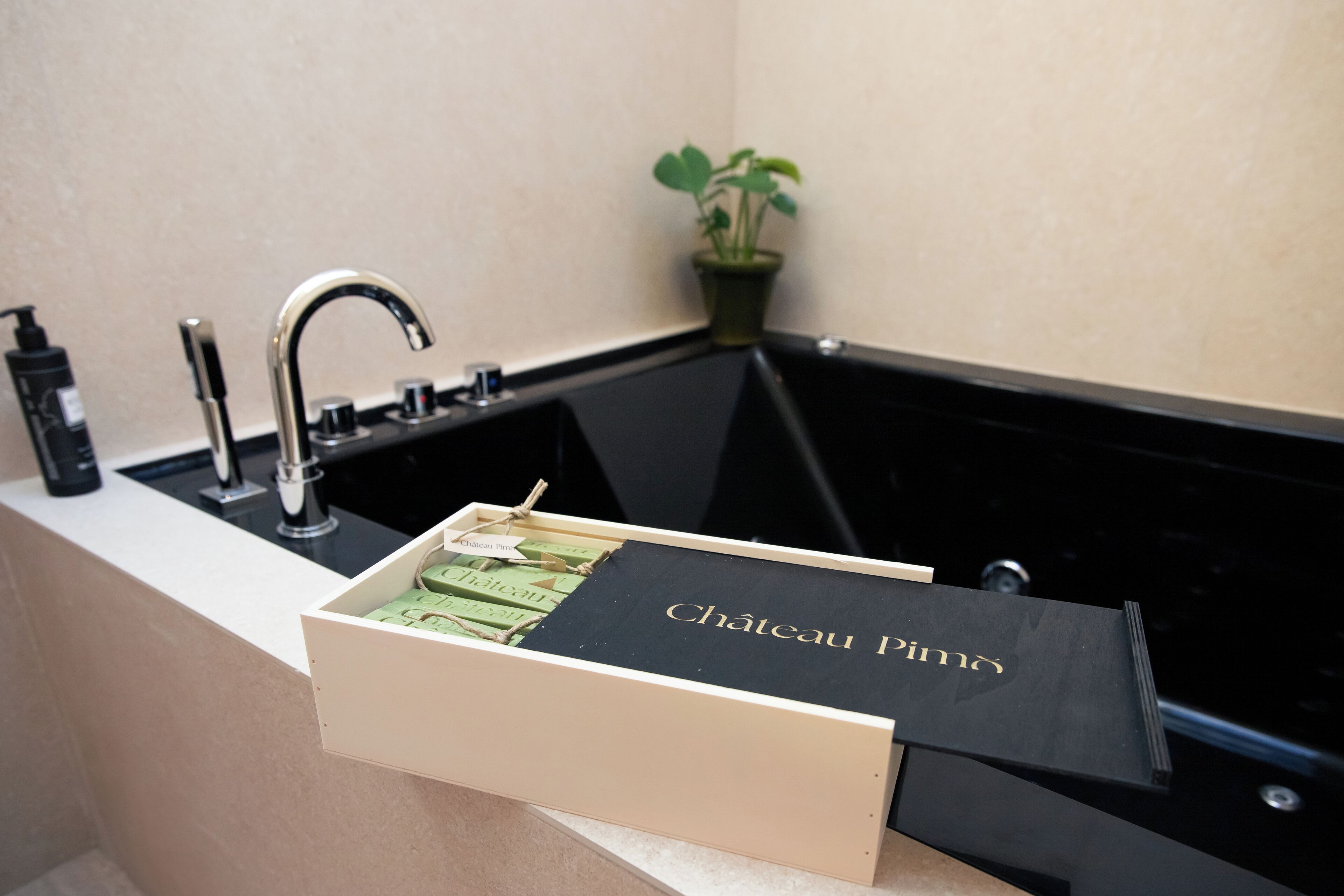 Un baño con una bañera negra, un lavabo y un cajón de madera con una caja negra etiquetada como "Chateau Pin".