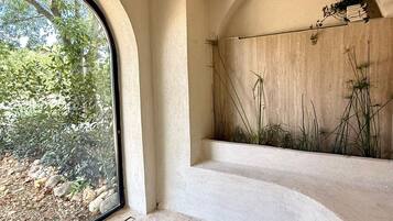Une pièce dotée d’une grande fenêtre en arc de cercle, d’un jardin intégré où poussent de hautes plantes et d’un sol recouvert de carreaux de pierre.