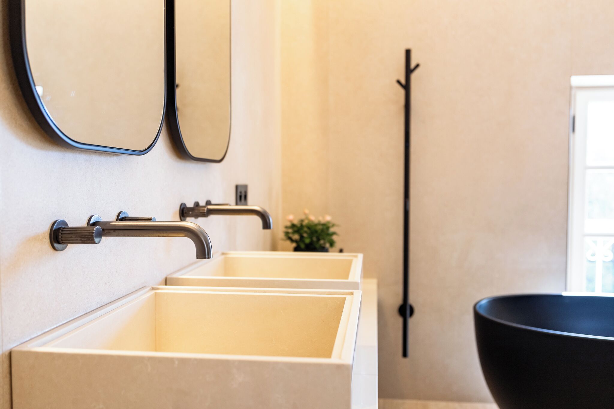 Un baño moderno con tres lavamanos rectangulares, una bañera negra y un espejo sobre los lavamanos.
