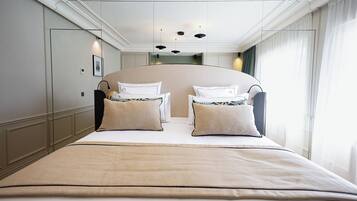 Un grand lit avec une couvre-lit beige, deux oreillers blancs et une tête de lit au design incurvé.