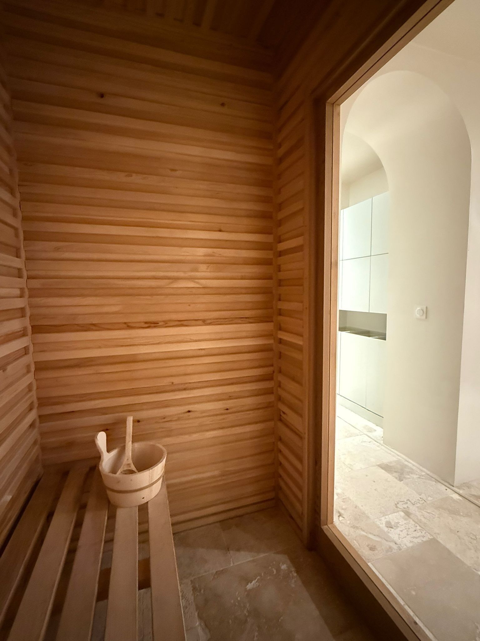 A wooden sauna room with a bench and a wooden bucket.