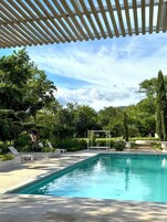 Un área de piscina con una pérgola, sillas de descanso y un jardín bien cuidado.