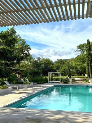 Ein Poolbereich mit Pergola, Liegestühlen und einem gepflegten Garten.