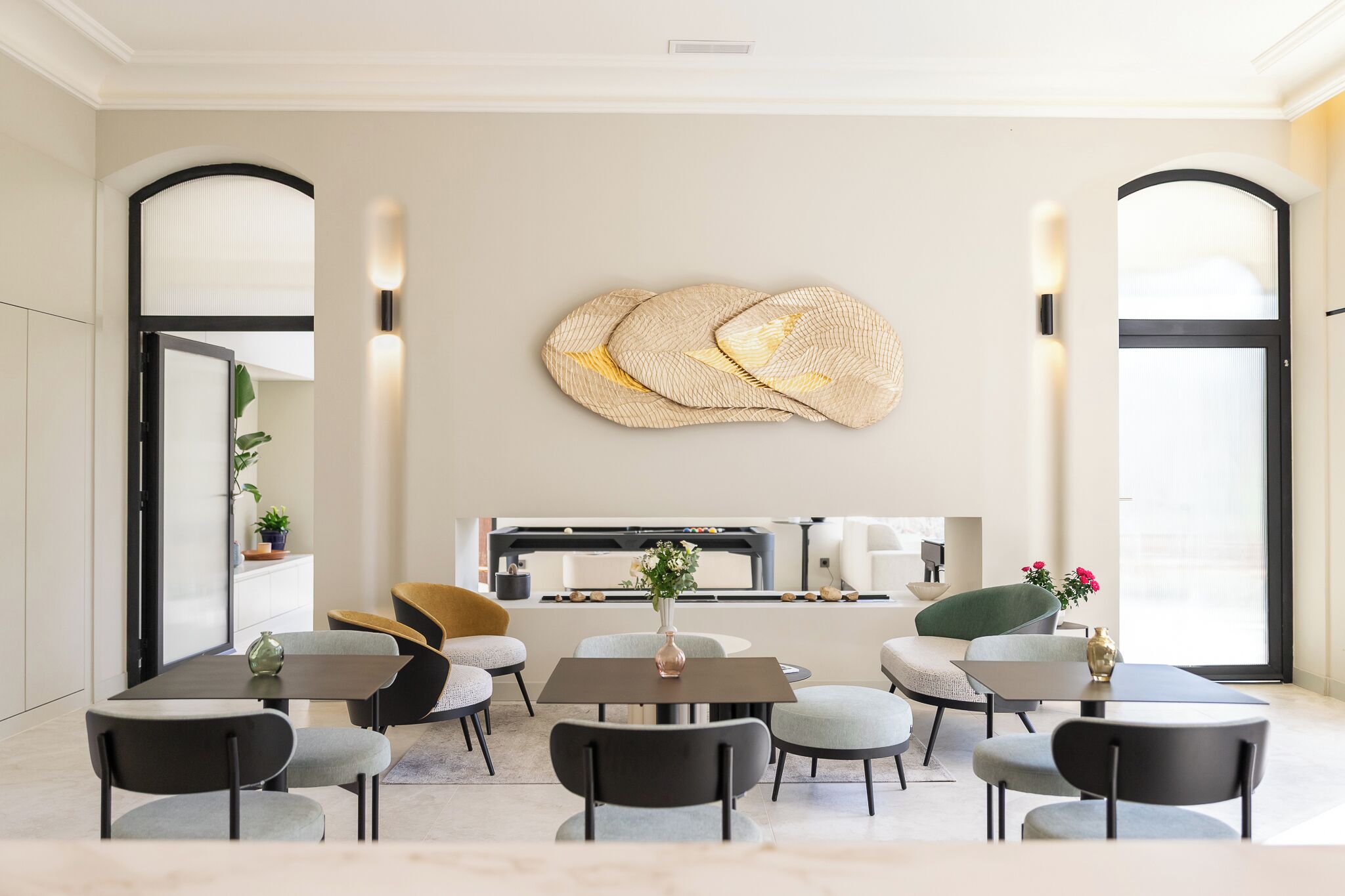 A modern dining area with a central table, surrounding chairs, and a decorative wall piece.