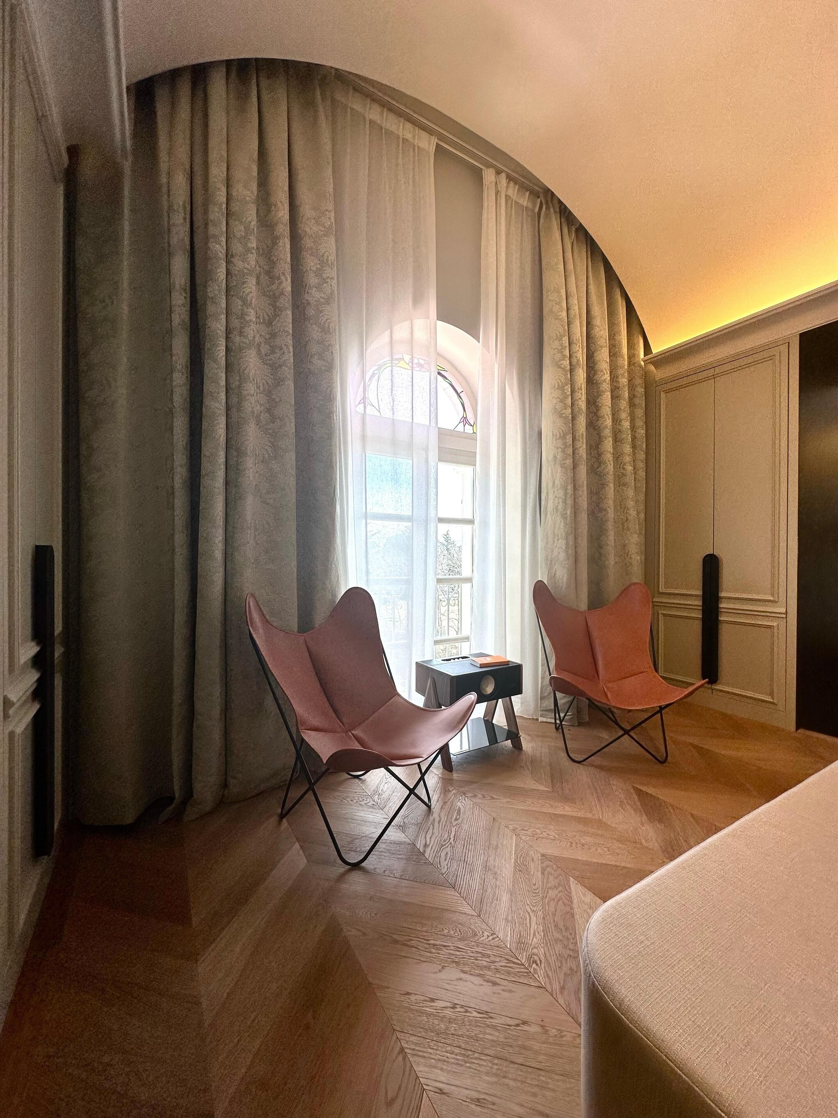 Una habitación con un ventanal grande, dos sillones, una mesita y una cama.