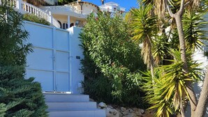 A set of stairs leading to a white gate, surrounded by greenery and rocks. - Magnificent Villa with swimming pool and panoramic view, ideal for 6 people. (Cumbre del Sol)