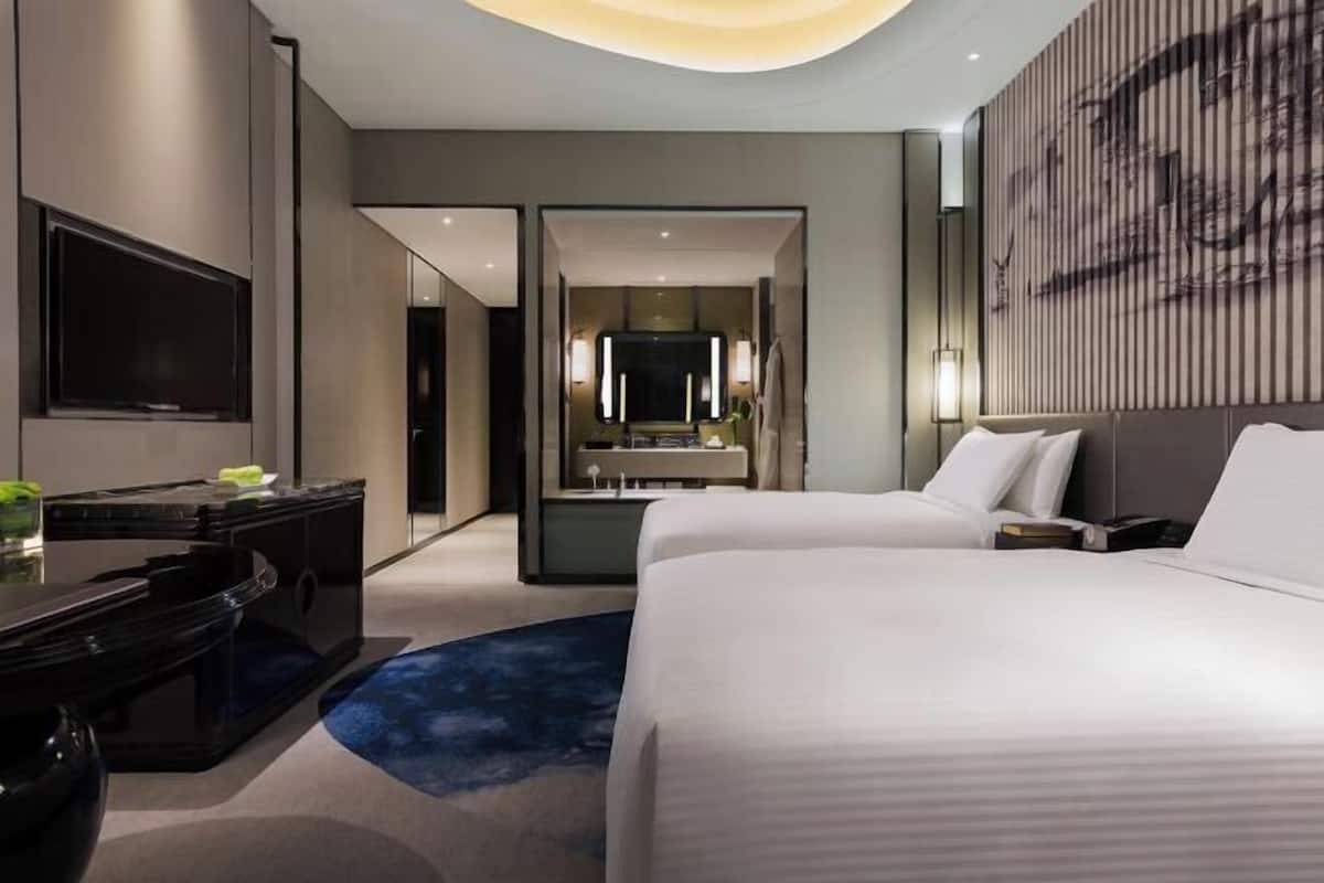 A modern hotel room with a large bed, a desk, a flat-screen TV, a mirror, and a wall-mounted artwork.